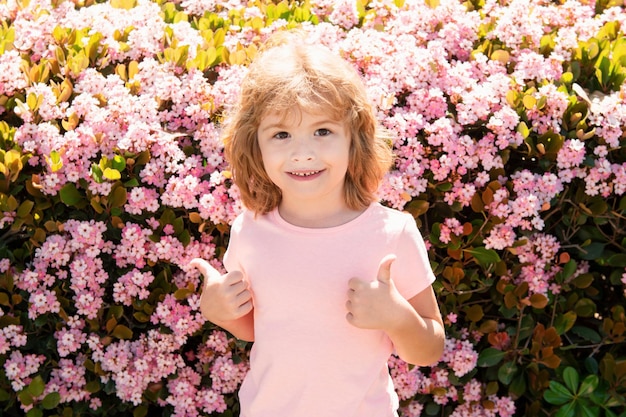 Niño caucásico en flor fondo de primavera Los niños se enfrentan a los pulgares para arriba