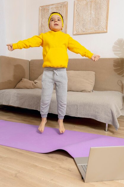 Niño caucásico haciendo ejercicios de fitness en casa Niño divirtiéndose durante el deporte Niño hace entrenamiento mirando la computadora Deporte yoga en línea Entrenamiento en el apartamento Estilo de vida saludable