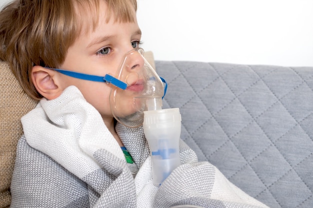 Niño caucásico haciendo inhalación con nebulizador en casa.