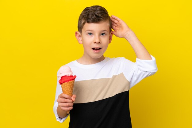 Un niño caucásico con un helado de cucurucho aislado de fondo amarillo con expresión de sorpresa