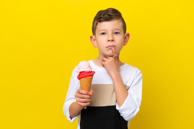 Un niño caucásico con un helado de cucurucho aislado en un fondo amarillo que tiene dudas mientras mira hacia arriba