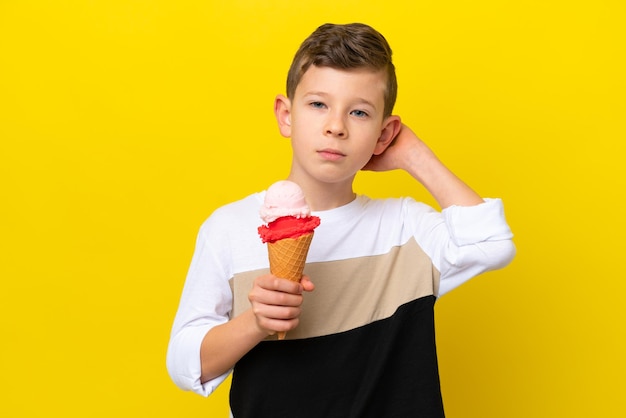Un niño caucásico con un helado de cucurucho aislado de fondo amarillo que tiene dudas