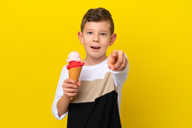 Un niño caucásico con un helado de cucurucho aislado de fondo amarillo sorprendido y apuntando al frente
