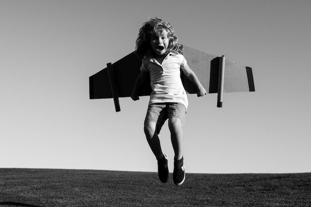 Niño caucásico jugando con un avión de juguete en el fondo del cielo afuera en una colina de verano cubierta de hierba soñando con