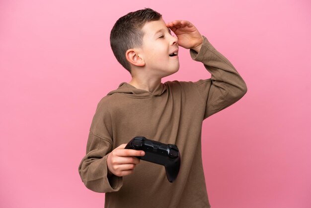 Un niño caucásico jugando con un controlador de videojuegos aislado en un fondo rosa sonriendo mucho