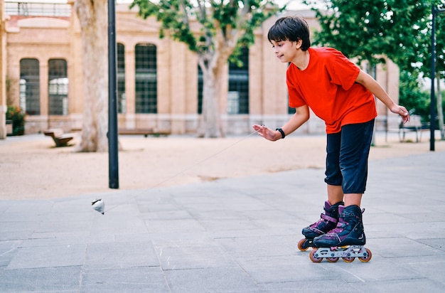 Foto niño caucásico jugando con patines y tirando peonza en el parque.