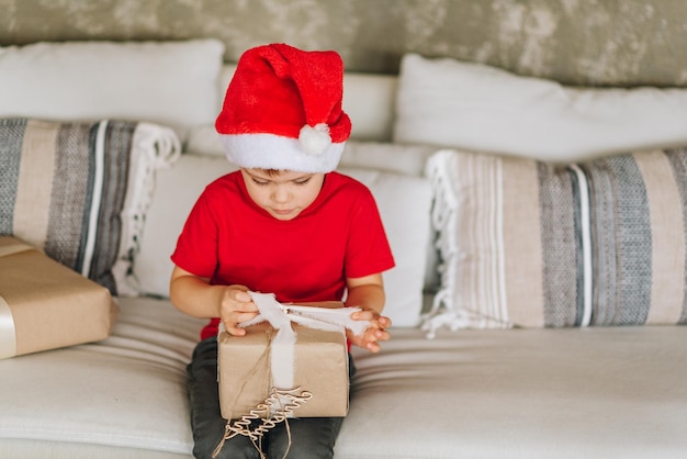 Niño caucásico riendo feliz en rojo Santa Claus recibiendo sus regalos en la mañana de Navidad Niño emocionado y sonriente Abriendo regalos Copiar espacio