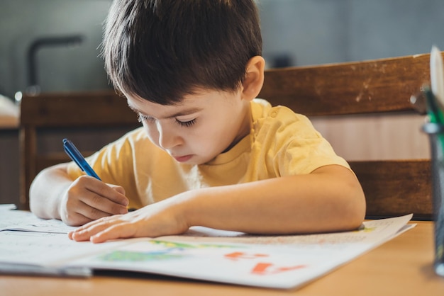 Niño caucásico sentado en la mesa y haciendo su tarea para la clase de la escuela primaria