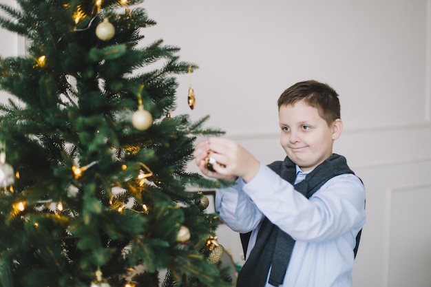 Niño caucásico sonriente decorando el árbol de Navidad en el interior de una casa y en un ambiente festivo