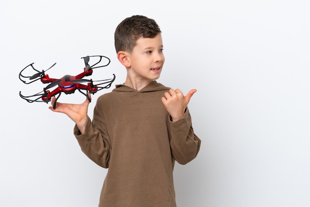 Niño caucásico sosteniendo un dron aislado de fondo blanco apuntando hacia un lado para presentar un producto