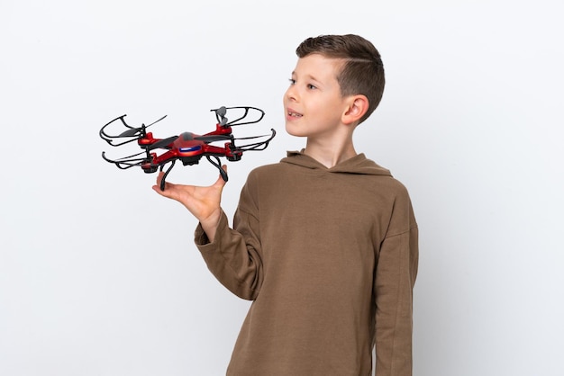 Niño caucásico sosteniendo un dron aislado de fondo blanco mirando hacia un lado y sonriendo