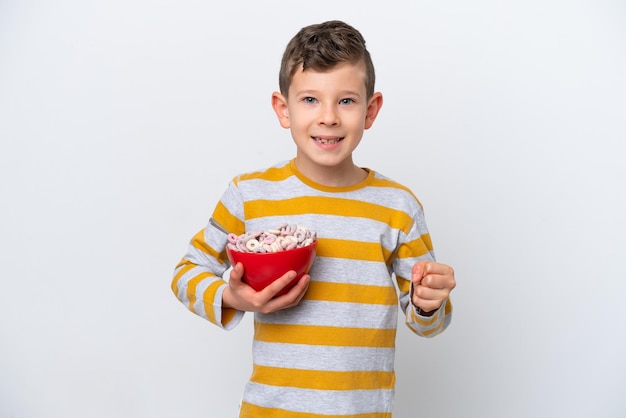 Un niño caucásico sosteniendo un tazón de cereal aislado de fondo blanco celebrando una victoria en posición de ganador