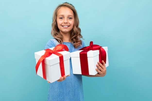 Niño caucásico tiene muchas cajas blancas con regalos y alegrías, retrato aislado en azul