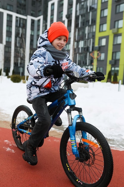 Un niño caucásico vestido con una chaqueta de invierno monta una bicicleta