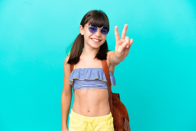 Un niño caucásico yendo a la playa aislado de fondo azul sonriendo y mostrando el signo de la victoria