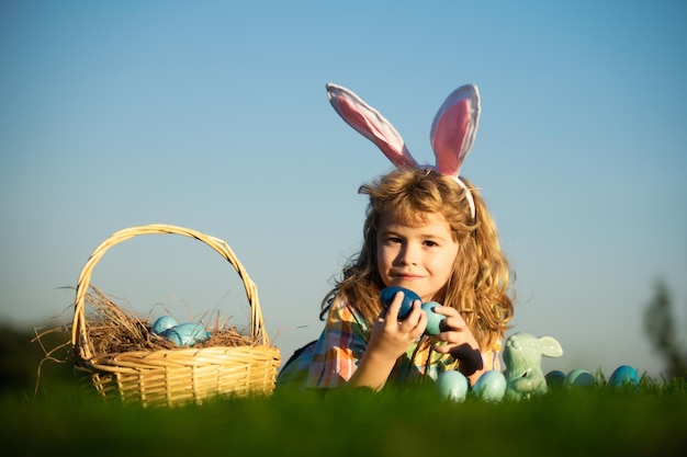 Niño cazando huevos de pascua en el patio trasero recostado sobre la hierba verde sobre fondo de cielo con espacio de copia