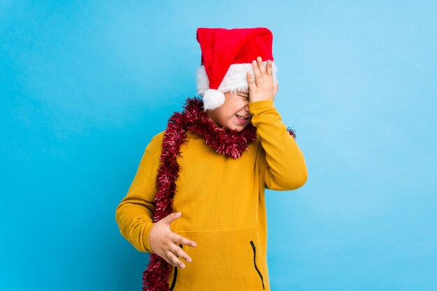 Niño celebrando el día de Navidad con un sombrero de santa aislado olvidando algo, golpeándose la frente con la palma y cerrando los ojos.