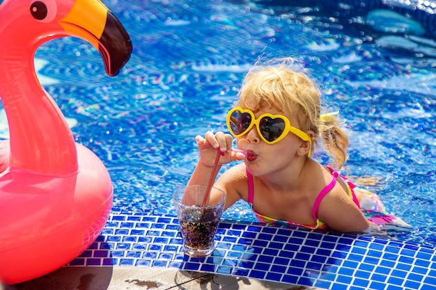 Un niño cerca de la piscina con gafas de sol bebiendo un cóctel enfoque selectivo