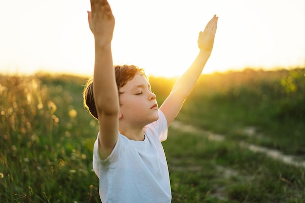 El niño cerró los ojos y rezó en un campo al atardecer. Las manos dobladas en concepto de oración por la fe, la espiritualidad y la religión.