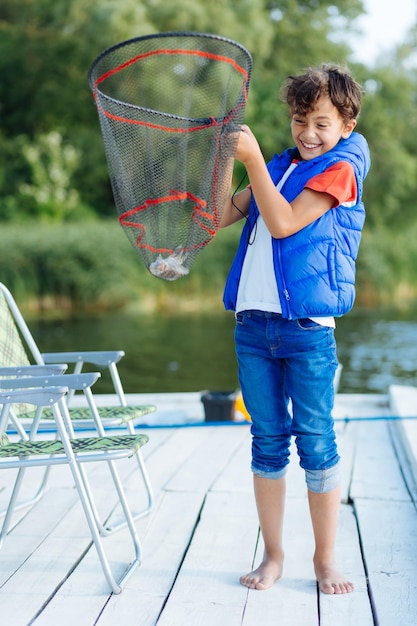 Foto niño con chaleco azul sintiéndose increíble después de pescar mientras sostiene la red