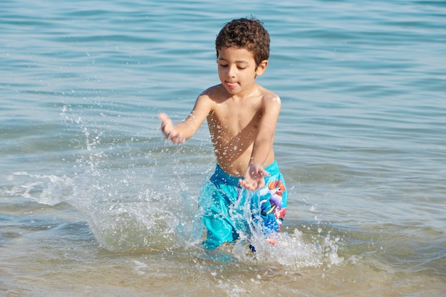 Un niño chapotea en el agua en una playa.