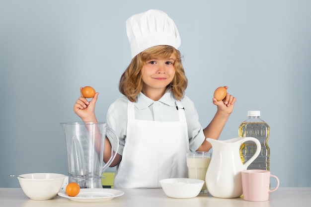 Niño chef aislado en azul sostener huevos divertido niño pequeño chef cocinero vistiendo uniforme gorro de cocinero y delantal