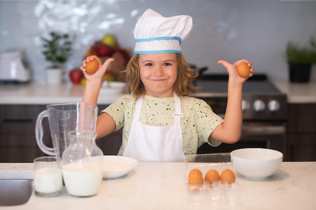 Niño chef cocinero con huevos en la cocina Cocina divertida para niños Un niño pequeño y divertido chef cocinero vistiendo uniforme gorro de cocinero y delantal comida cocinada en la cocina Los niños están preparando comida para hornear galletas en la cocina