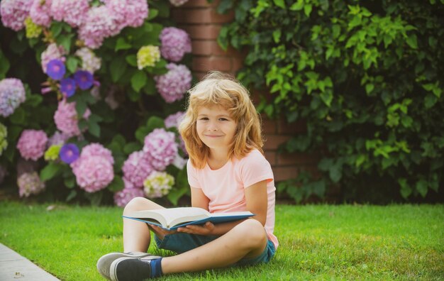 Niño chico leyendo un libro tirado en la hierba Lindo niño pequeño en ropa casual leyendo un libro y sonriendo