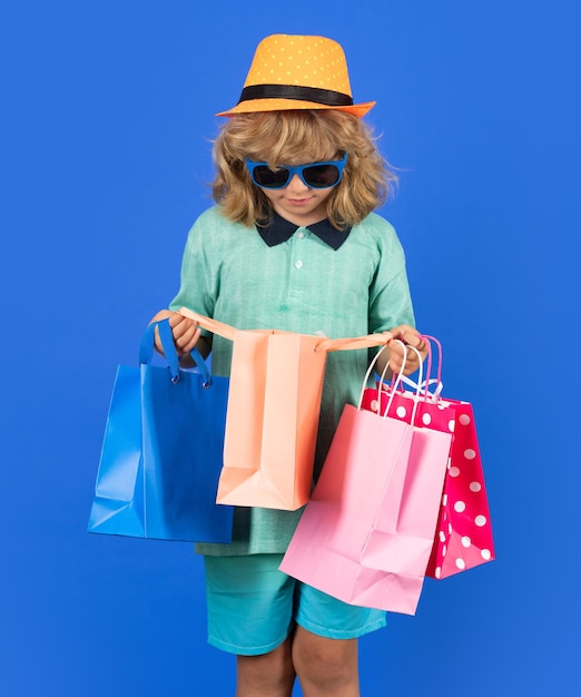 Niño chico en ropa de moda va de compras Niño con paquetes de compras Shopper niño con transporte