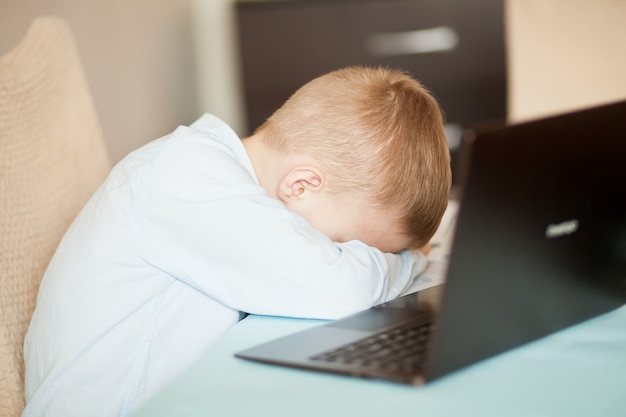 Niño chico sentado en el escritorio con un portátil portátil tableta digital. estaba muy cansado y se durmió. niño aprendiendo en línea. educación a distancia en línea.