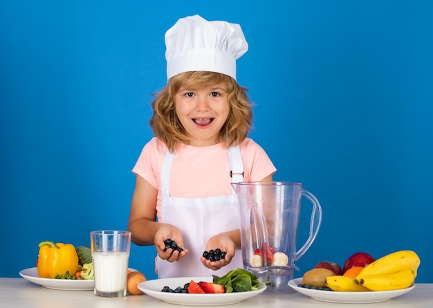 Niño chico con sombrero de chef y delantal cocinando batido de arándanos pequeño cocinero con verduras en la cocina na