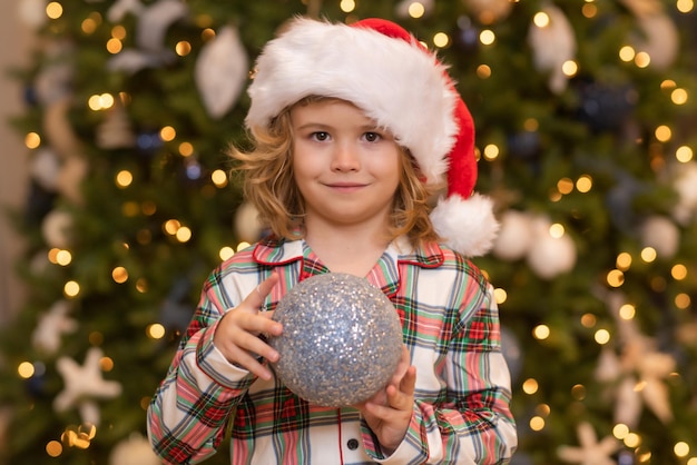 Niño chico con sombrero de santa cerca del árbol de navidad en casa