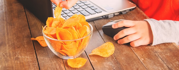 Niño con chips detrás de una computadora. enfoque selectivo