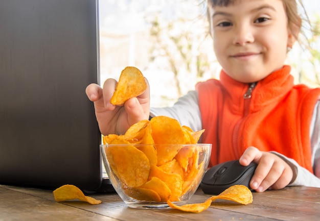 Niño con chips detrás de una computadora