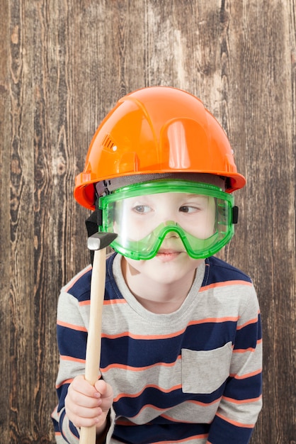 Un niño de cinco años con un casco y sostiene un martillo en la mano mientras enseña construcción, un plan de cortina