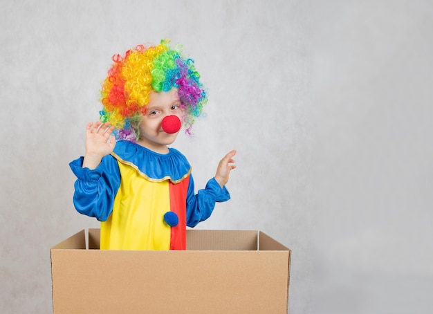 Niño de cinco años vestido con el traje de payaso se queda en una caja de cartón. De cerca