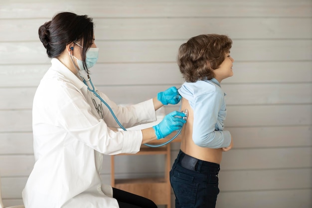 Un niño en la clínica del médico del terapeuta en el examen, el médico escucha los pulmones