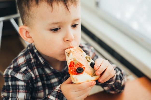 El niño en la cocina de casa comiendo pizza con salmón