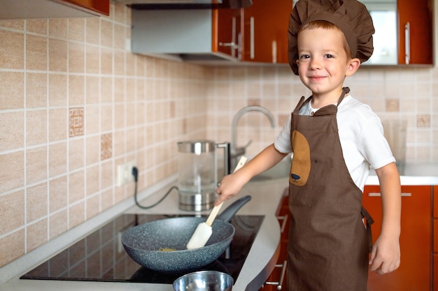 Niño cocina comida en casa en la cocina mirando a la cámara.