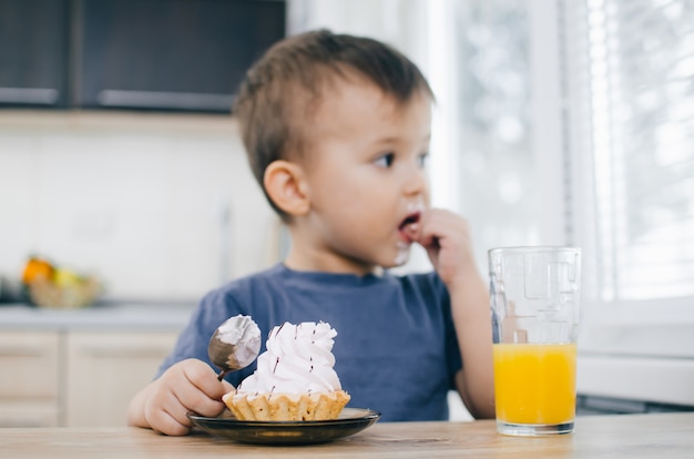 El niño en la cocina comiendo un pastel con crema.