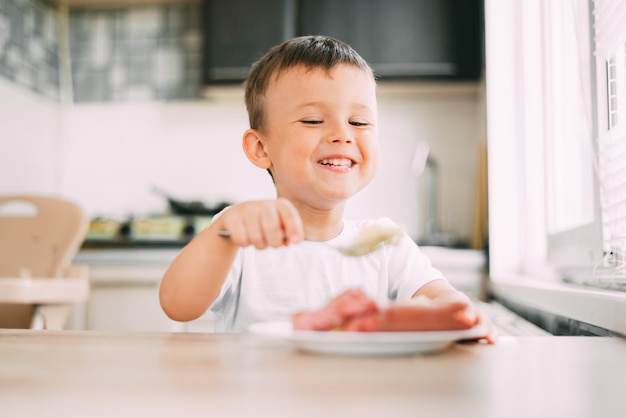 el niño en la cocina comiendo salchichas y puré de papas solo