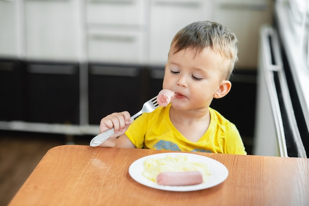 Niño en la cocina comiendo salchichas y puré de papas