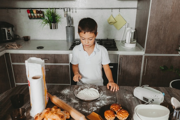 Niño en la cocina haciendo masa. niño ayuda a mamá en la cocina.