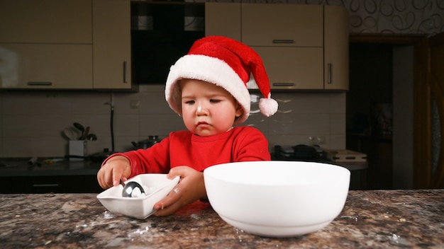 Niño en la cocina con un sombrero de Navidad. Foto de alta calidad