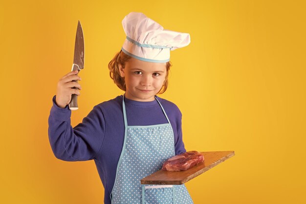 Foto niño cocinero sostenga la tabla de cortar con carne bistec y cuchillo chef niño niño haciendo comida saludable retrato de niño pequeño en sombrero de chef aislado en el fondo del estudio