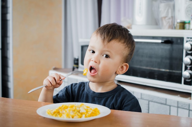 el niño codiciosamente en la cocina comiendo una tortilla por la tarde en el verano