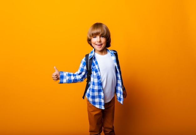 Niño colegial mostrando los pulgares para arriba aislado sobre fondo amarillo