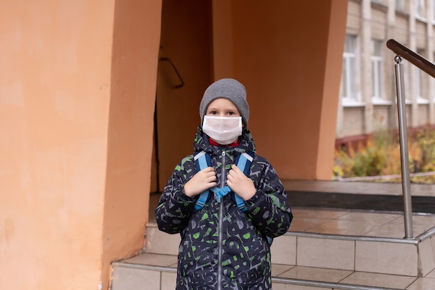 Niño colegial sale de la escuela con máscara protectora