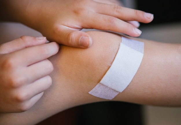 Foto un niño se coloca una tirita en la piel dañada de la pierna. una abrasión y un rasguño en la rodilla. primera atención médica en casa.