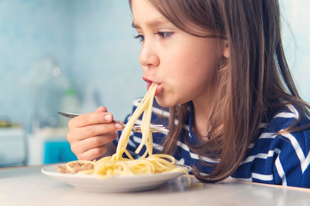 El niño come ansiosamente una deliciosa pasta en la cocina.